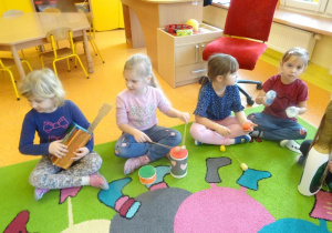 Czwórka dzieci siedzi z instrumentami muzycznymi wykonanymi z materiałów pochodzących z recyklingu.